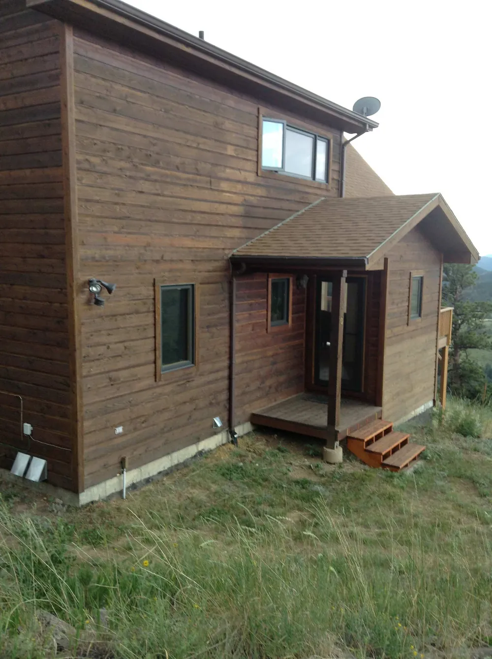 Back of a mountain home with stained cedar siding and a small porch