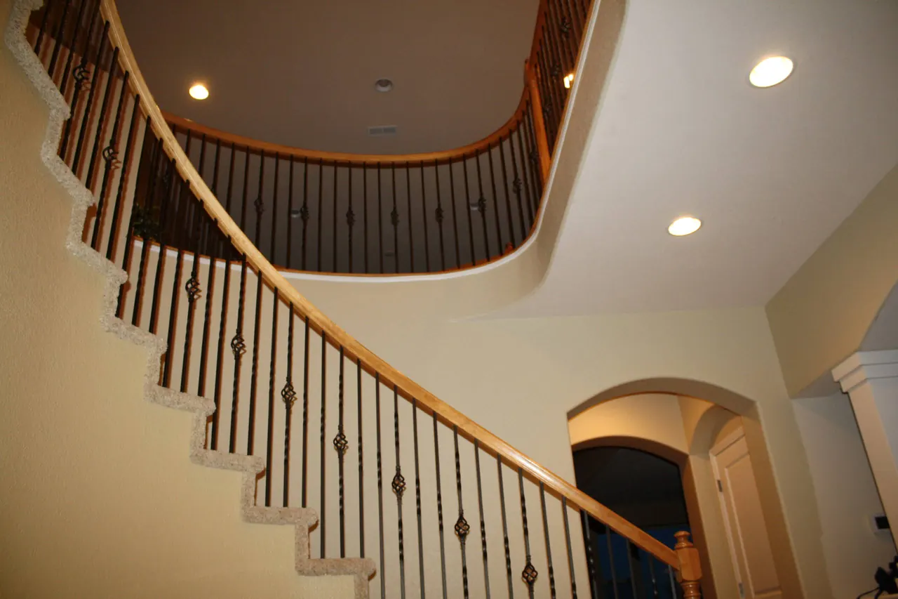 Curved staircase with a stained handrail and iron balusters